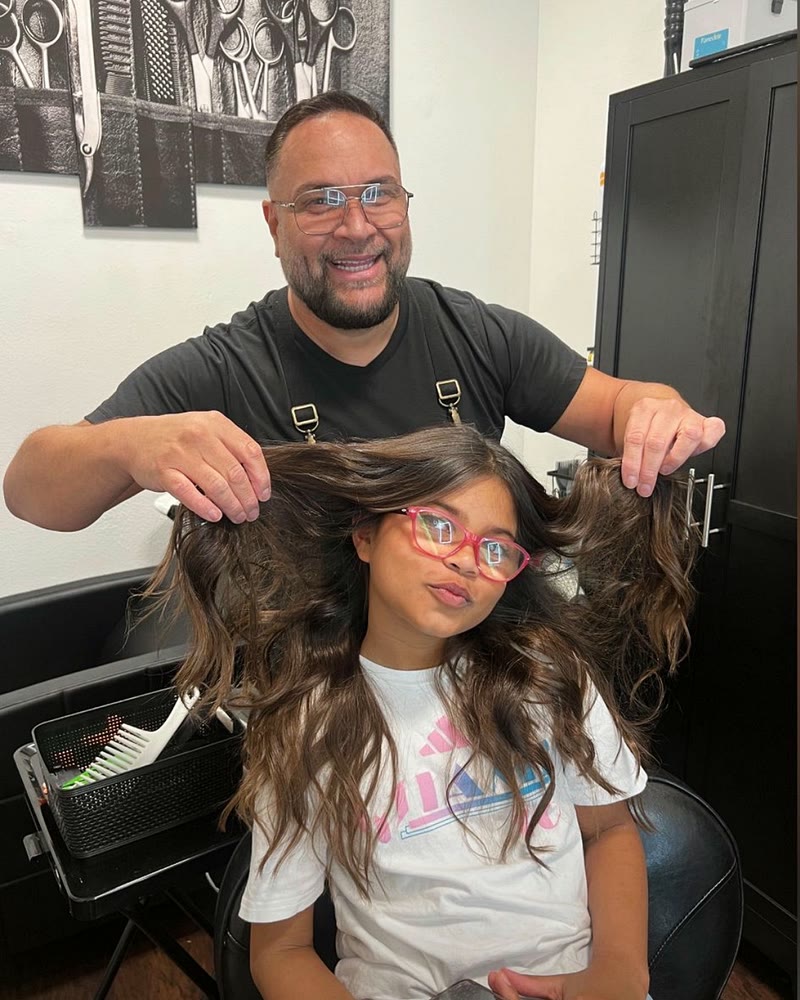 Stylist showing a young client's long, wavy brunette hair at Will Vazquez Beauty Bar, Orlando